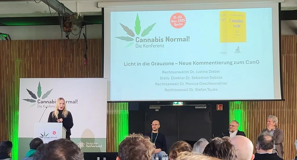 Advocate Dr. Justine Diebel bespreekt tijdens CaNoKo 2025 verschillende invalshoeken en nieuwe uitspraken in het Duitse consumentenrecht. Ze staat op een podium in de hoofdzaal van Alte Münze achter een sprekersgestoelte.